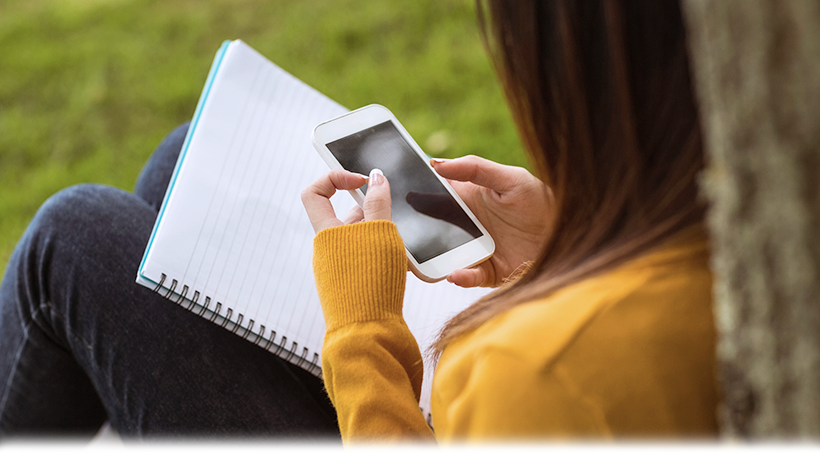 image of girl holding a cell phone device and sitting against a tree image of girl holding a cell phone device and sitting against a tree