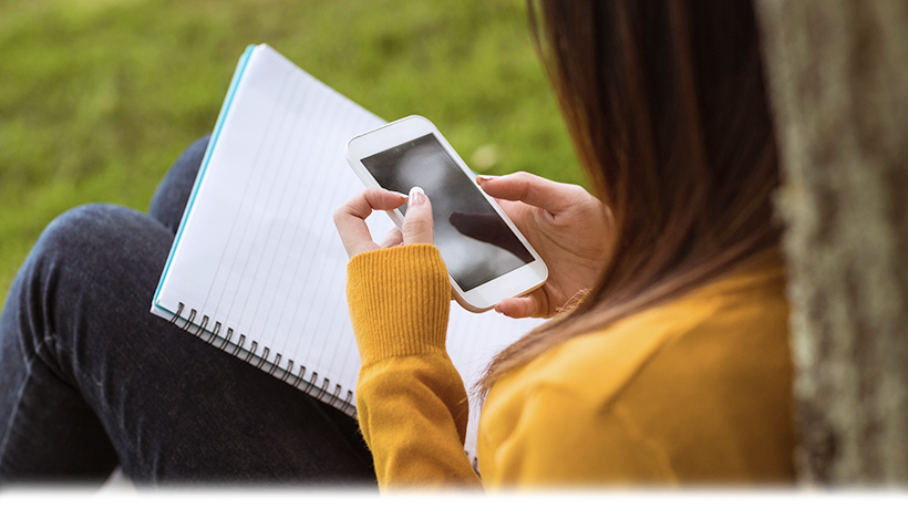 image of girl holding a cell phone device and sitting against a tree